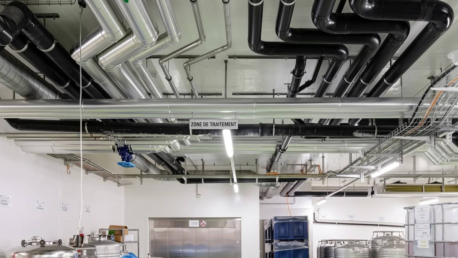 Tubazioni per il freddo preisolate nere e linee in acciaio inox a soffitto in un locale di produzione con serbatoi inox